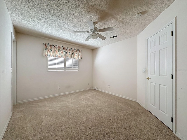 spare room featuring visible vents, baseboards, a ceiling fan, light colored carpet, and a textured ceiling