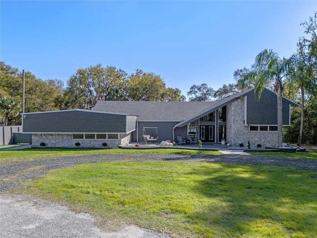 mid-century home featuring stone siding and a front lawn