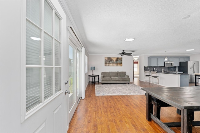 living room featuring a textured ceiling, a ceiling fan, light wood-style flooring, and crown molding