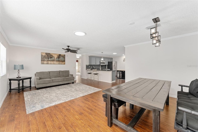 dining area featuring a textured ceiling, a ceiling fan, light wood-style flooring, and crown molding