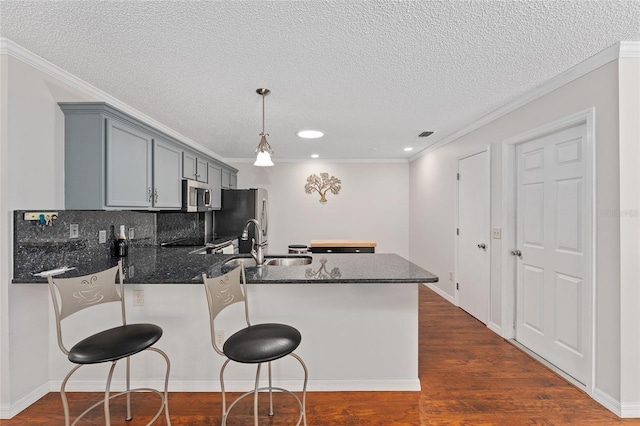 kitchen featuring dark wood finished floors, stainless steel appliances, backsplash, a sink, and a peninsula