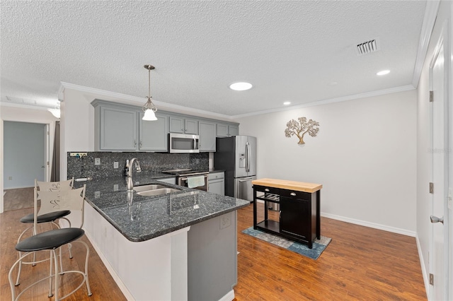 kitchen with a breakfast bar area, backsplash, appliances with stainless steel finishes, a sink, and wood finished floors