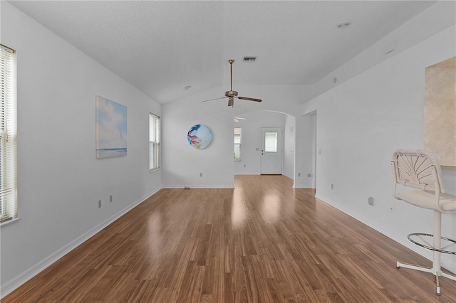 unfurnished living room featuring arched walkways, plenty of natural light, wood finished floors, and visible vents