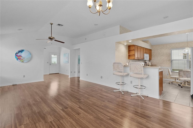 unfurnished living room featuring ceiling fan with notable chandelier, visible vents, vaulted ceiling, and wood finished floors