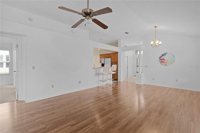 unfurnished living room with visible vents, lofted ceiling, light wood-style flooring, a textured ceiling, and ceiling fan with notable chandelier