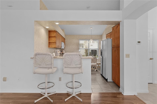 kitchen featuring open shelves, brown cabinetry, freestanding refrigerator, a peninsula, and a kitchen bar