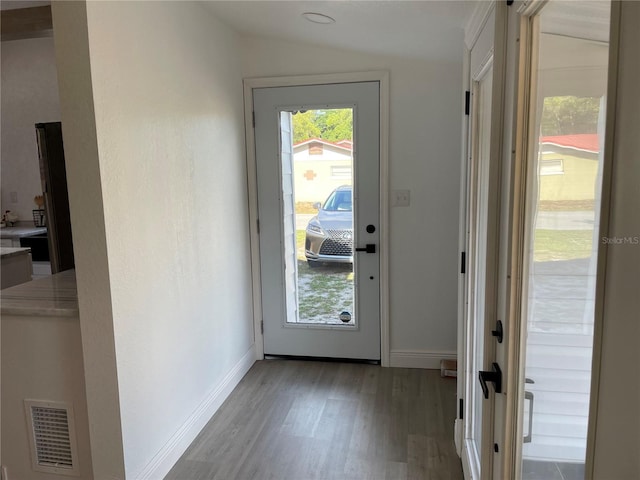 doorway to outside with baseboards, visible vents, vaulted ceiling, and wood finished floors