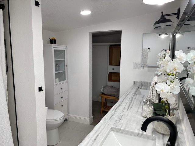 bathroom with double vanity, baseboards, toilet, tile patterned flooring, and a sink