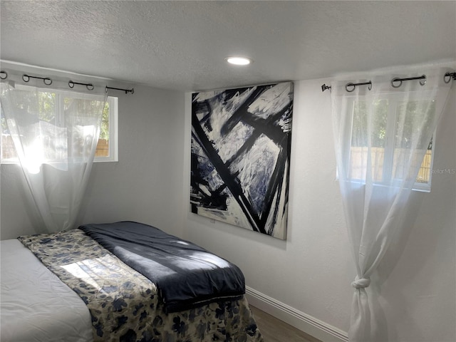 bedroom featuring a textured ceiling, baseboards, and wood finished floors