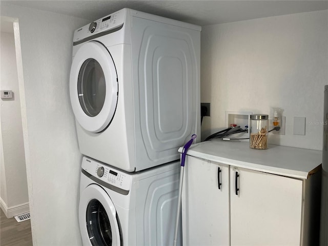 laundry area with cabinet space, baseboards, visible vents, stacked washer / dryer, and wood finished floors