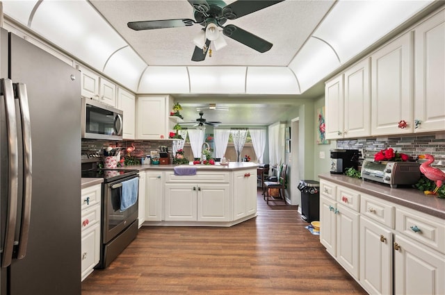 kitchen with stainless steel appliances, a peninsula, dark wood finished floors, and white cabinetry