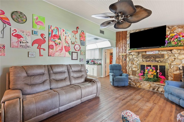 living room with ceiling fan, a stone fireplace, wood finished floors, and visible vents