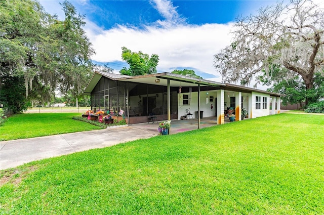 rear view of property featuring concrete driveway, a yard, an attached carport, and a sunroom