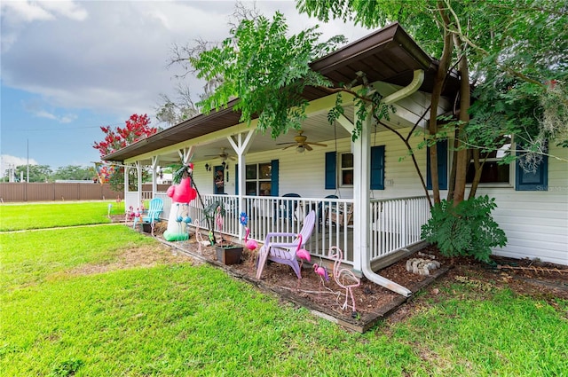 view of front facade with covered porch, ceiling fan, a front lawn, and fence