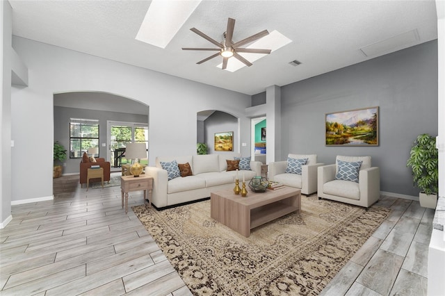 living room featuring wood finish floors, a skylight, visible vents, and baseboards