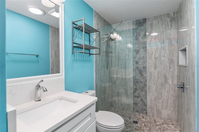 bathroom with tiled shower, a textured ceiling, toilet, and vanity