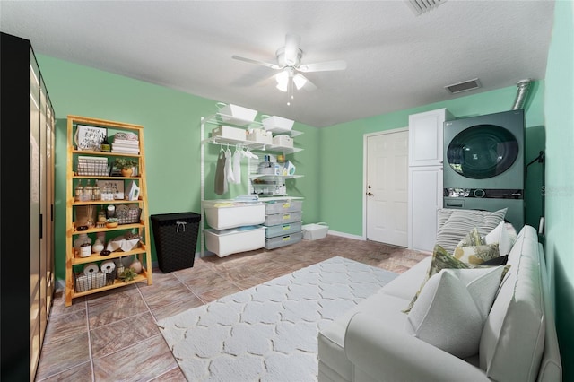 interior space featuring ceiling fan, a textured ceiling, stacked washing maching and dryer, and visible vents