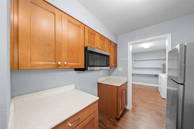 kitchen featuring brown cabinetry, stainless steel appliances, dark wood-type flooring, and separate washer and dryer