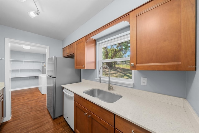kitchen featuring brown cabinetry, white dishwasher, freestanding refrigerator, a sink, and dark wood-type flooring