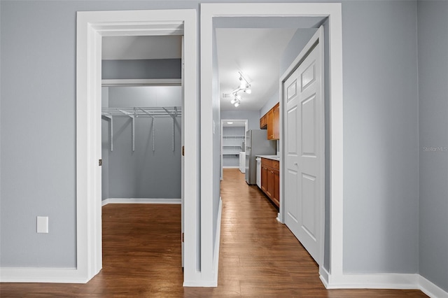 hall featuring dark wood-type flooring, baseboards, and track lighting
