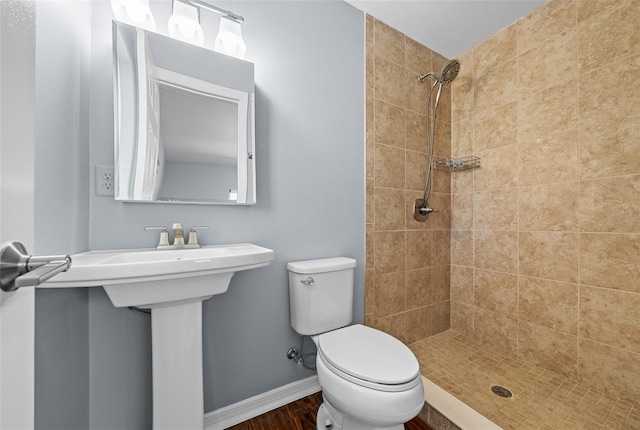 full bathroom with toilet, tiled shower, baseboards, and wood finished floors