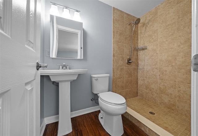 bathroom with baseboards, toilet, wood finished floors, and a tile shower