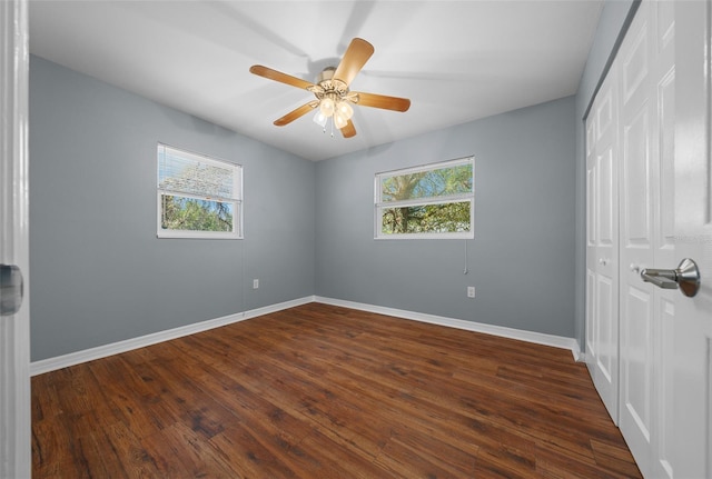 unfurnished bedroom with multiple windows, baseboards, a closet, and dark wood-style flooring