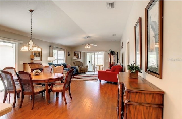 dining room featuring visible vents, vaulted ceiling, light wood-style flooring, and ceiling fan with notable chandelier