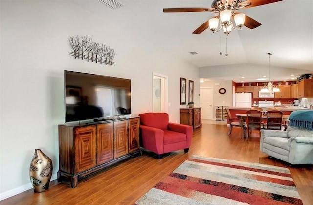 living area with baseboards, visible vents, ceiling fan, wood finished floors, and vaulted ceiling