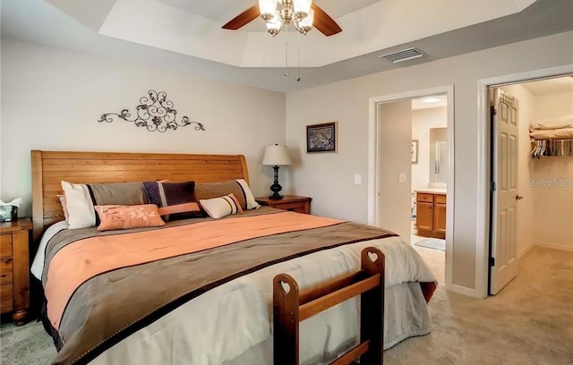 bedroom with a raised ceiling, visible vents, a spacious closet, light carpet, and ensuite bath