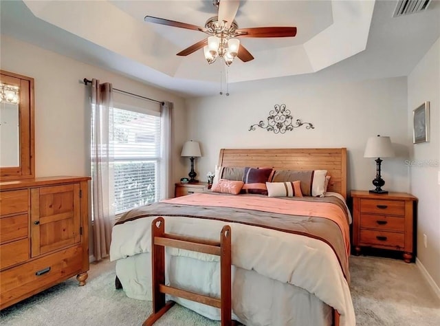 bedroom with baseboards, visible vents, light colored carpet, ceiling fan, and a tray ceiling