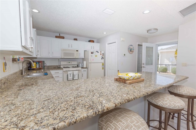 kitchen with white appliances, visible vents, a peninsula, white cabinetry, and a sink