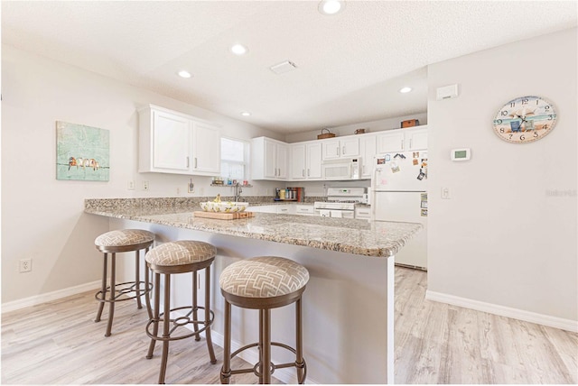 kitchen featuring white appliances, light wood finished floors, a breakfast bar, a peninsula, and white cabinetry