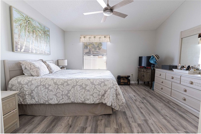 bedroom featuring lofted ceiling, a textured ceiling, a ceiling fan, and wood finished floors