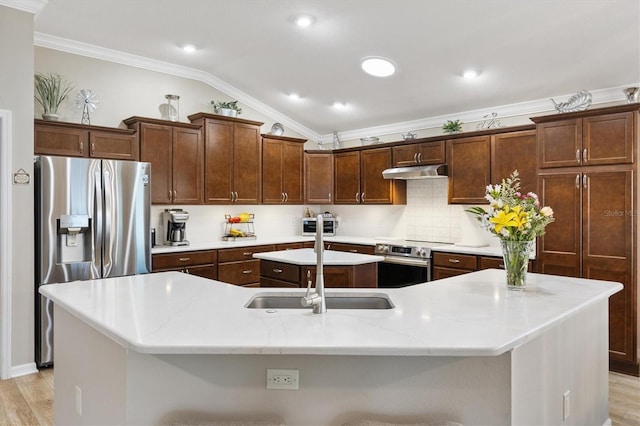 kitchen with under cabinet range hood, vaulted ceiling, appliances with stainless steel finishes, a center island with sink, and crown molding