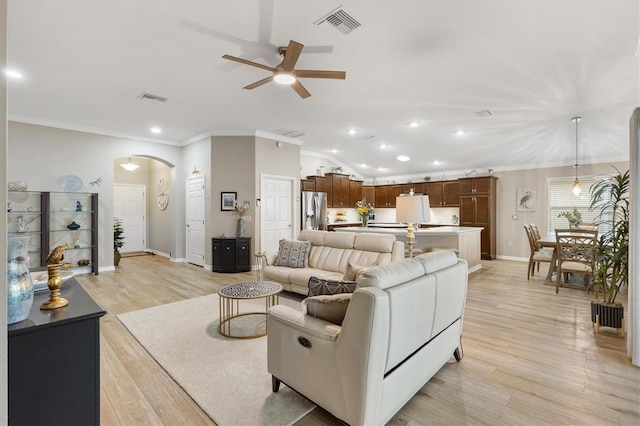 living area featuring light wood-type flooring, visible vents, arched walkways, and ornamental molding