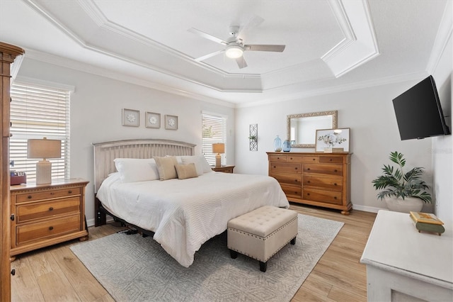 bedroom featuring baseboards, light wood finished floors, a raised ceiling, and crown molding