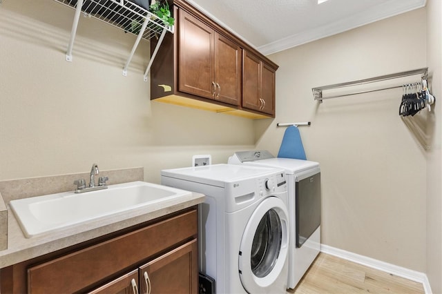 laundry area with washing machine and dryer, a sink, light wood-style floors, cabinet space, and crown molding