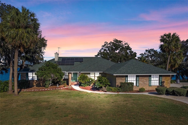 view of front facade featuring brick siding, a yard, a chimney, and solar panels