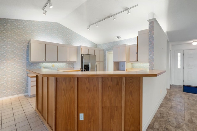 kitchen with wallpapered walls, stainless steel fridge, vaulted ceiling, and light countertops