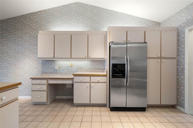 kitchen featuring wallpapered walls, light tile patterned floors, stainless steel fridge with ice dispenser, lofted ceiling, and cream cabinetry