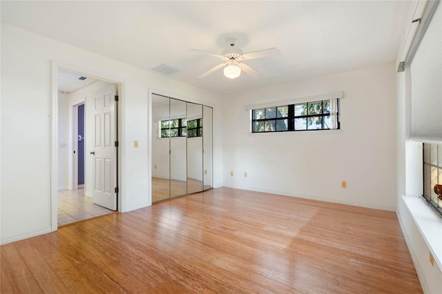 unfurnished bedroom with light wood-style flooring, multiple windows, ceiling fan, and a closet