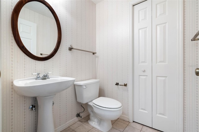 half bathroom with tile patterned floors, toilet, a sink, baseboards, and wallpapered walls