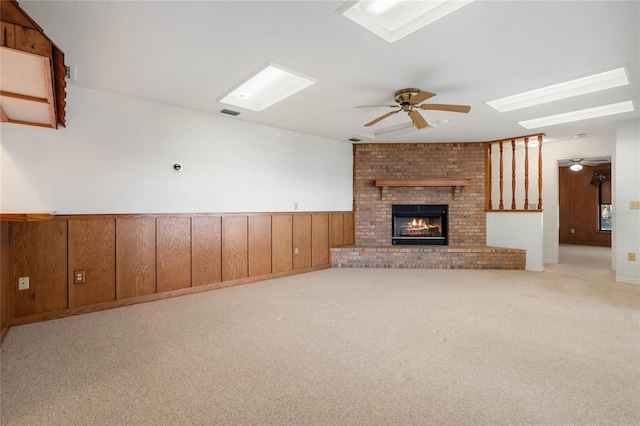 unfurnished living room with a wainscoted wall, ceiling fan, carpet floors, and a fireplace