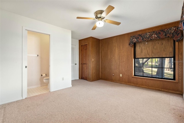 unfurnished bedroom with wooden walls, baseboards, a ceiling fan, ensuite bath, and carpet