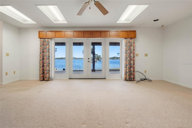 carpeted spare room with french doors, a water view, a ceiling fan, and baseboards