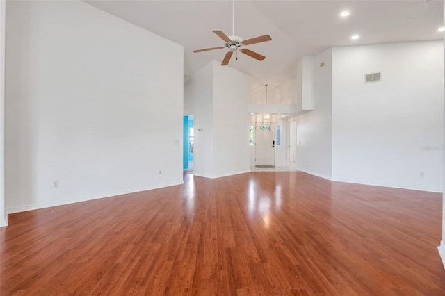 unfurnished living room with ceiling fan, high vaulted ceiling, wood finished floors, visible vents, and baseboards