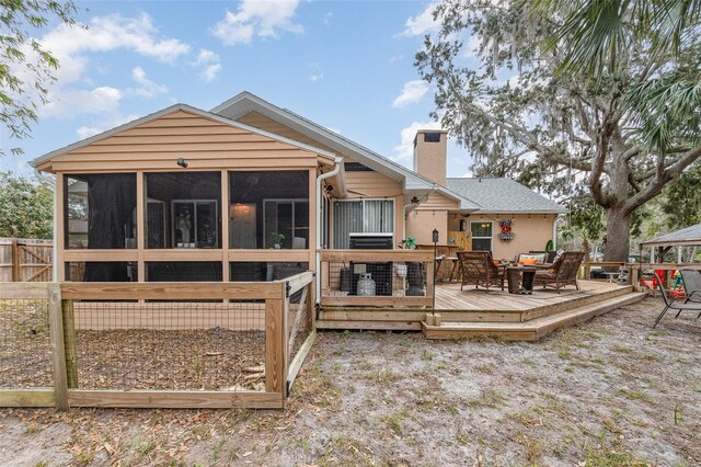 back of house featuring a chimney, a wooden deck, and a sunroom