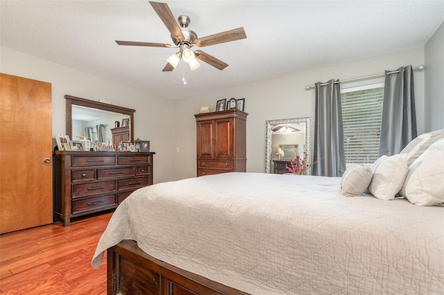 bedroom with a textured ceiling, light wood-style flooring, and a ceiling fan