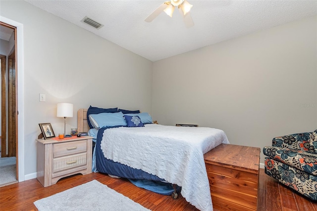 bedroom featuring baseboards, visible vents, ceiling fan, wood finished floors, and a textured ceiling